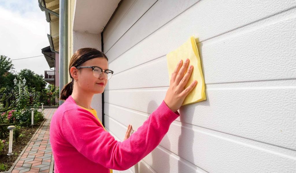 Homeowner cleaning garage door panels with soap and soft brush during regular maintenance routine