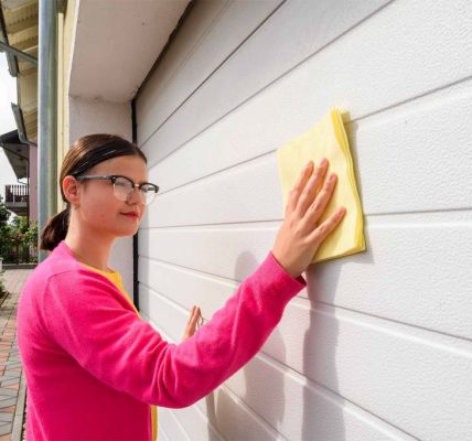 Homeowner cleaning garage door panels with soap and soft brush during regular maintenance routine