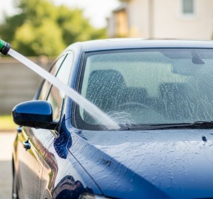 Person rinsing a car with a garden hose using a gentle water stream from top to bottom