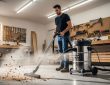 A man using a large garage vacuum to clean sawdust and debris from a workshop floor